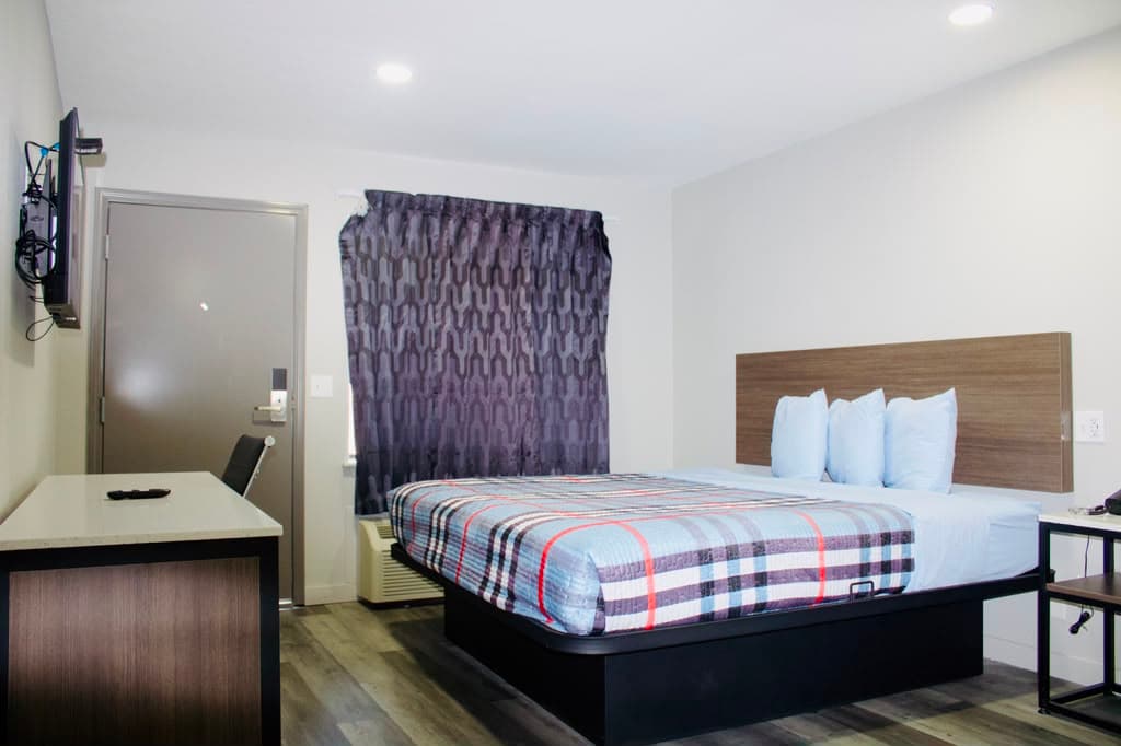 Full suite view: bed, desk, TV, and in-room climate control